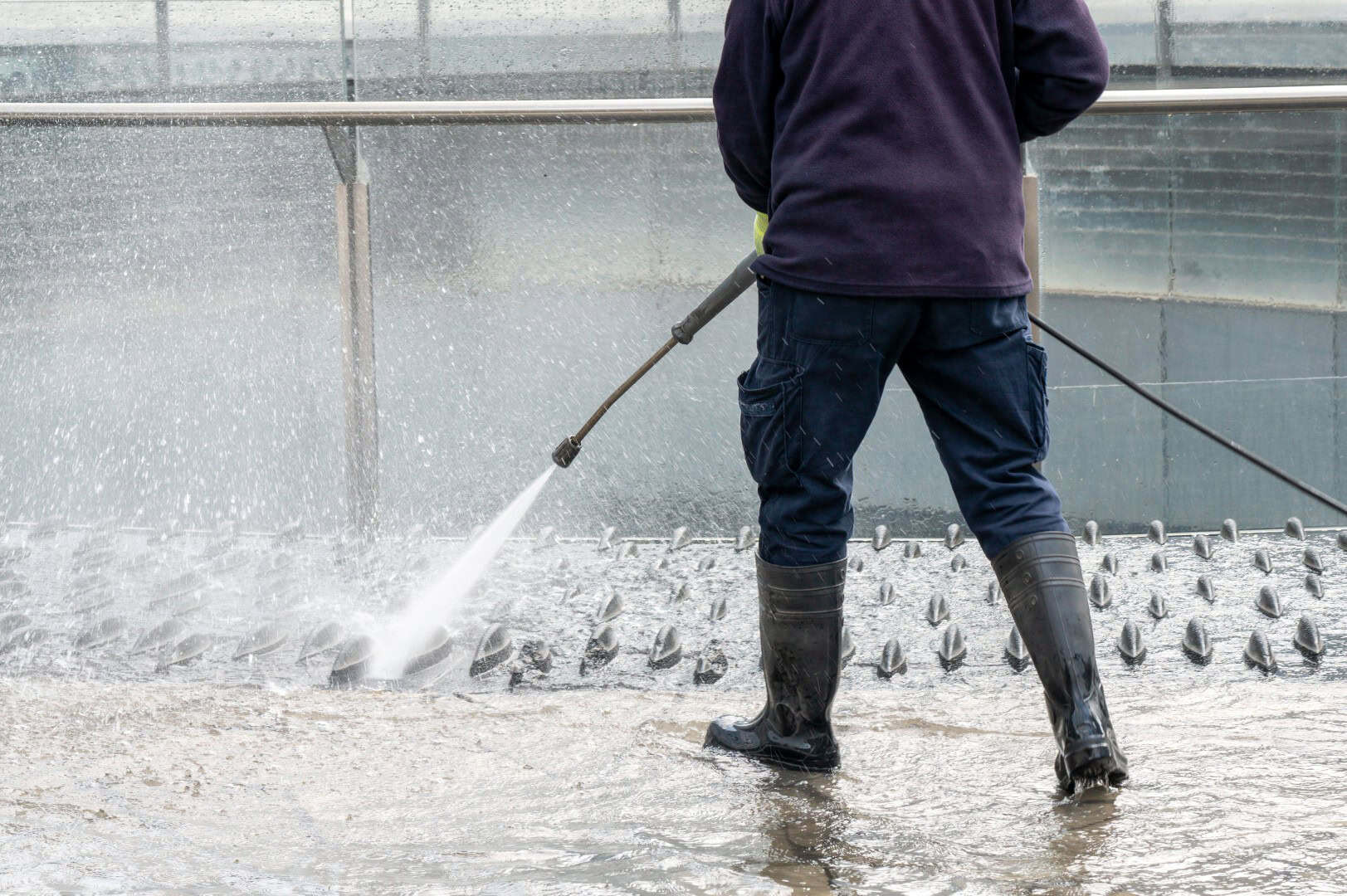 Person spraying strong stream of water to clean concrete floor and metal structures